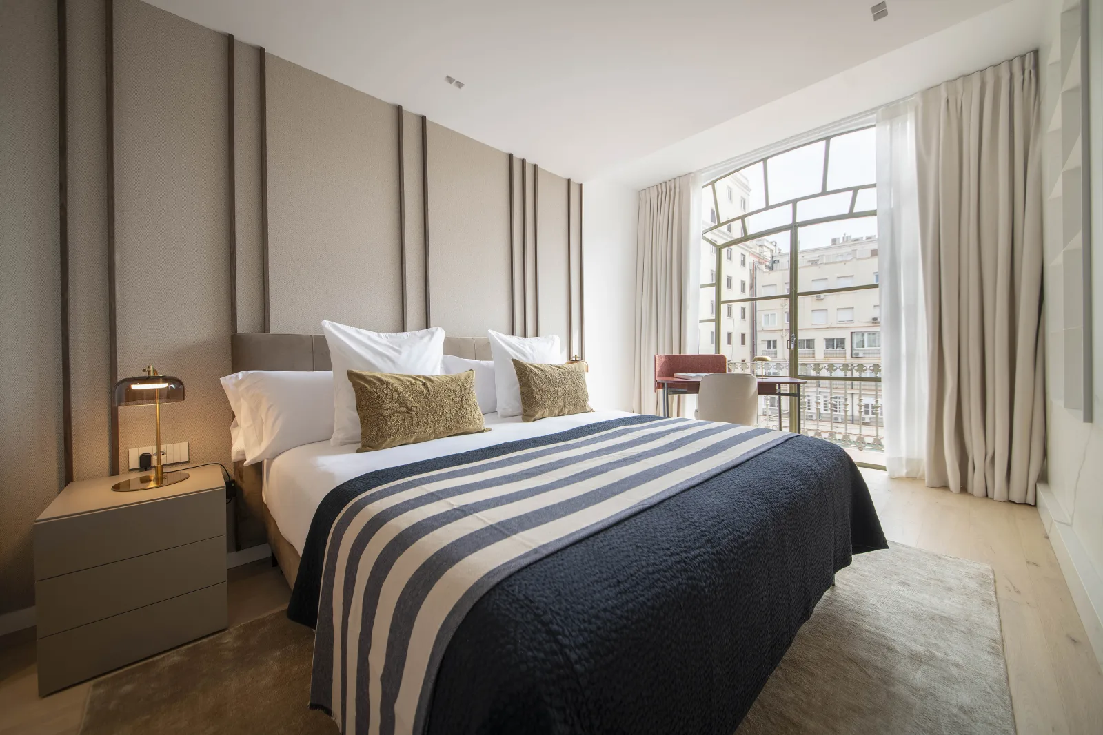 Suite Prestige principal bedroom with striped bedding and a city-facing window